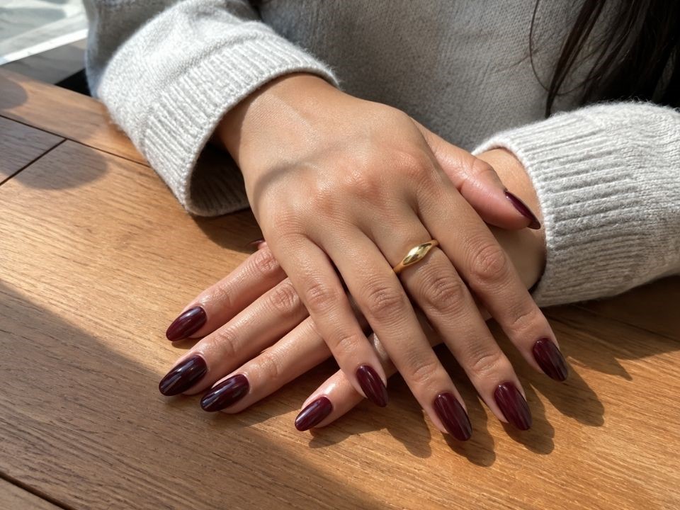 A flawless, glossy almond-shaped press-on nail manicure in deep burgundy color, looking like a professional salon job