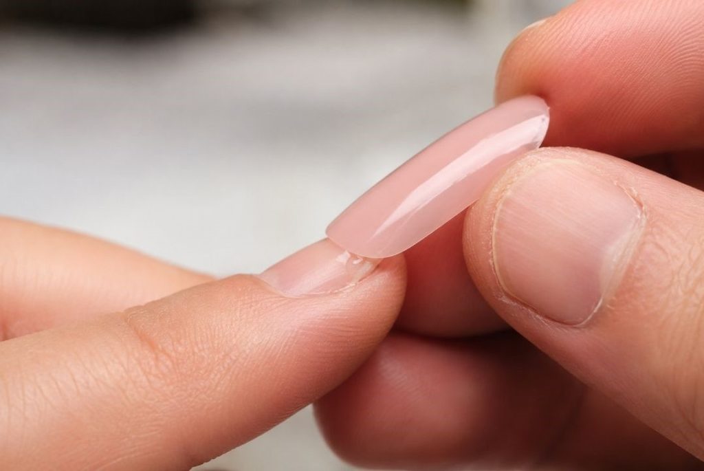 A macro shot showing the application of a press-on nail onto a natural nail using liquid glue at a 45-degree angle
